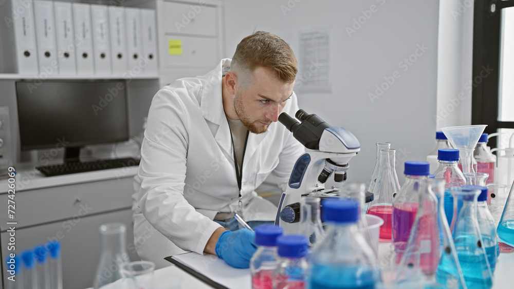 A young caucasian man with a beard works diligently in a laboratory, analyzing samples through a microscope. A young caucasian man with a beard works diligently in a laboratory, analyzing samples through a microscope.