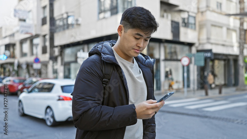 Принти на полотні Handsome asian man using smartphone on a bustling city street, portraying urban lifestyle and connectivity