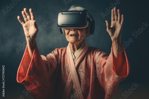 An elderly Asian woman in virtual reality glasses with her hands raised on a gray background