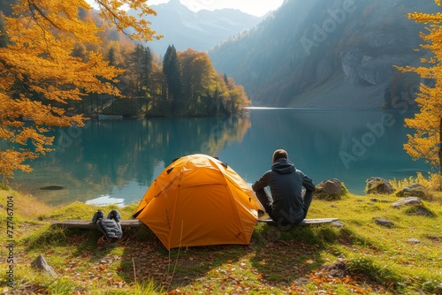 A lone hiker rests by the tranquil lake, surrounded by vibrant autumn foliage and equipped for a peaceful night under the starry sky