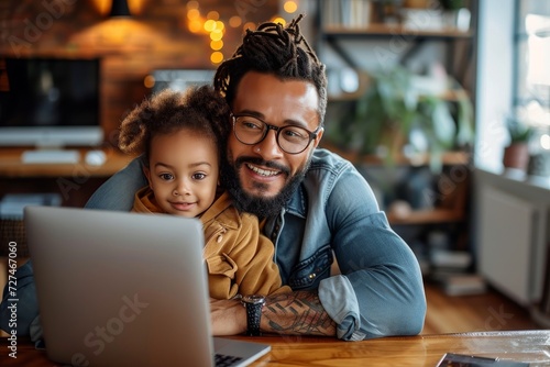 A young woman sits at a table with a smile on her face, her child by her side, as they both gaze at the laptop screen, surrounded by indoor furniture and walls, showcasing the intimate bond between a