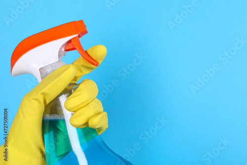 Woman holding plastic spray bottle on light blue background, closeup. Space for text