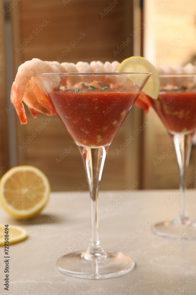 Tasty shrimp cocktail with sauce in glasses and lemon on light marble table Tasty shrimp cocktail with sauce in glasses and lemon on light marble table