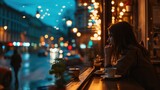 A young girl sitting in coffee shop with night street with historic buildings in the city of Prague, Czech Republic in Europe.