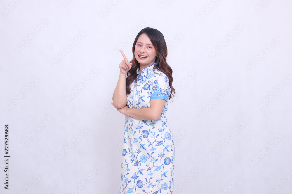 Beautiful smile asian woman wearing modern chinese dress arms crossed pointing right up isolated on white background. happy Chinese New Year