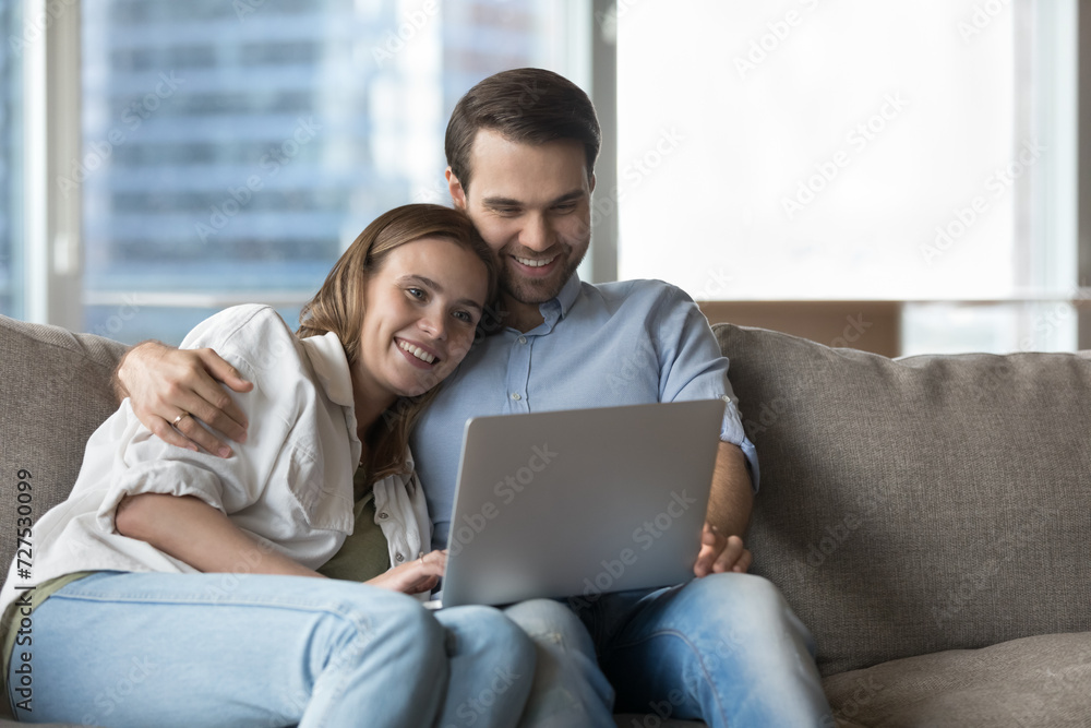 Couple in love resting on sofa watch online movie on laptop. Spouses spend carefree weekend on cozy couch, video calling to family using application, choose goods for home buying in e-commerce website