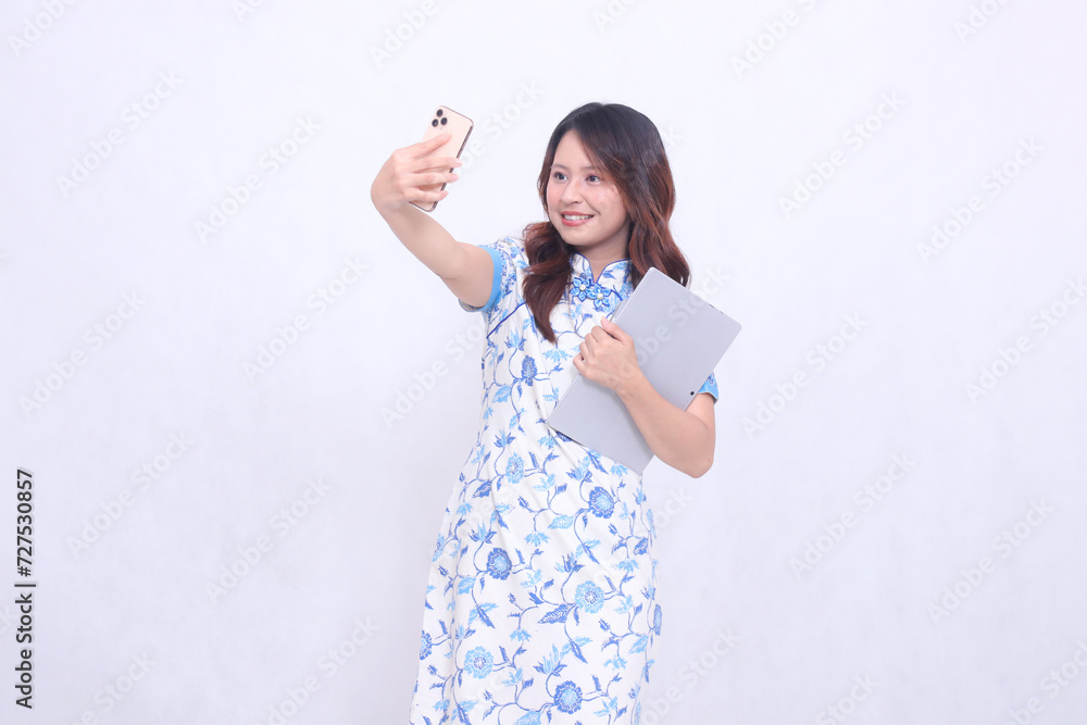beautiful asian woman wearing modern chinese blue dress obliquely cheerful holding tablet and photo looking at cellphone isolated white background beautiful asian woman wearing modern chinese blue dress obliquely cheerful holding tablet and photo looking at cellphone isolated white background