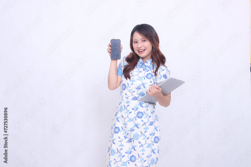 beautiful asian girl wearing blue chinese dress cheerful smile holding tablet and looking at cell phone screen isolated white background beautiful asian girl wearing blue chinese dress cheerful smile holding tablet and looking at cell phone screen isolated white background