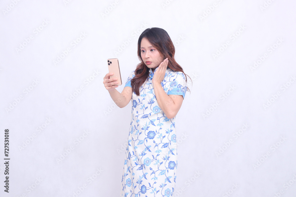 young asian javanese chinese woman shocked fascinated wearing blue chinese dress looking at cellphone and operating it isolated white background young asian javanese chinese woman shocked fascinated wearing blue chinese dress looking at cellphone and operating it isolated white background