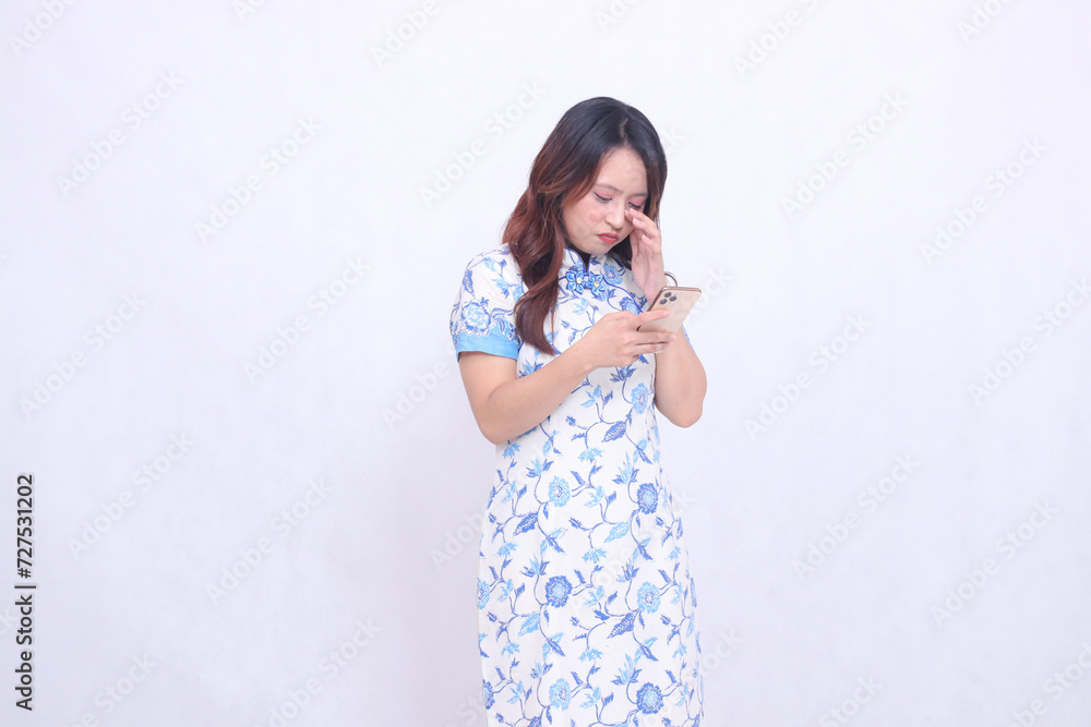 young Asian Javanese Chinese woman wearing blue Chinese dress pouting crying crookedly while focusing on typing on cell phone isolated white background young Asian Javanese Chinese woman wearing blue Chinese dress pouting crying crookedly while focusing on typing on cell phone isolated white background