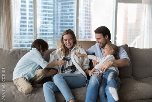Loving parents play with two siblings at home. Young mother and father enjoy funny playtime with preschoolers son and daughter, laughing, tickling each other, feel overjoyed. Family games and leisure