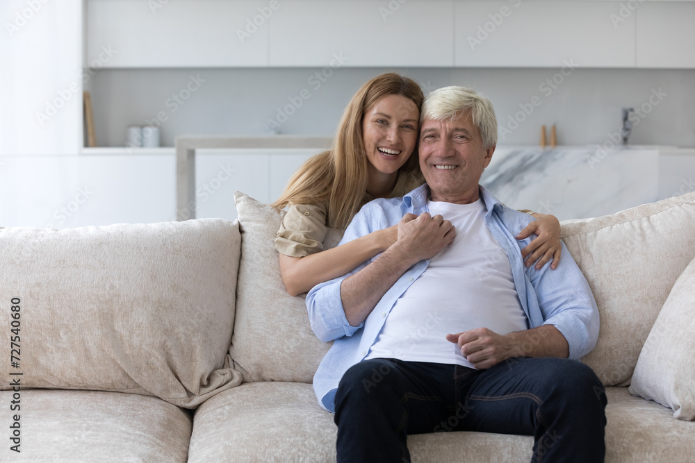 Happy pretty adult daughter woman hugging mature older dad with love, support, care, looking at camera, smiling. Senior father and grownup child home portrait