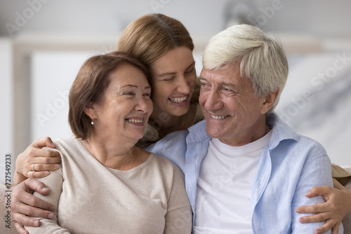 Cheerful adult daughter woman having fun with elder mom and dad, hugging with love, care, talking to parents, laughing, chatting, enjoying good family relationship, meeting at home