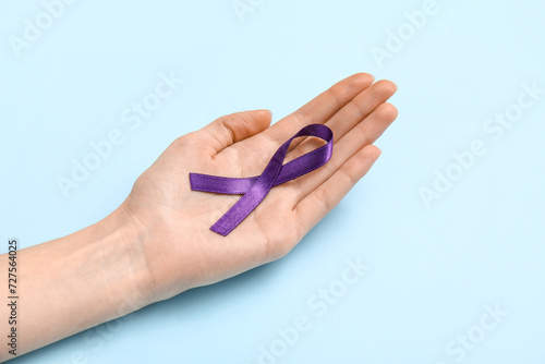 Female hand with purple ribbon on blue background. Cancer awareness concept