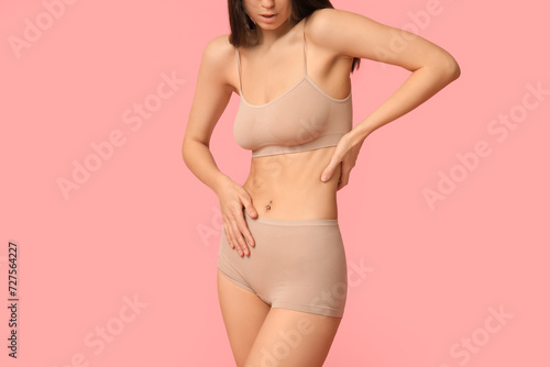 Beautiful young woman in beige underwear on pink background