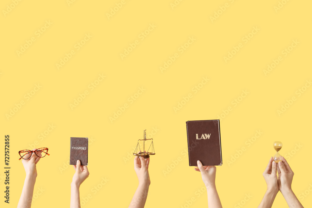 Female hands holding hourglass, scales of justice, law book and passport on yellow background Female hands holding hourglass, scales of justice, law book and passport on yellow background