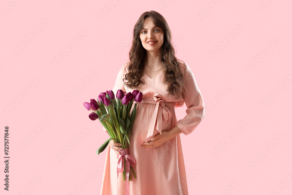 Young pregnant woman with bouquet of beautiful purple tulips on pink background