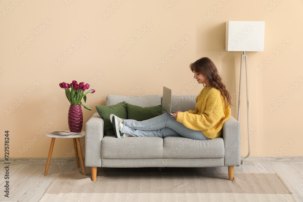 Pretty young woman using modern laptop and vase with bouquet of beautiful tulips at home Pretty young woman using modern laptop and vase with bouquet of beautiful tulips at home