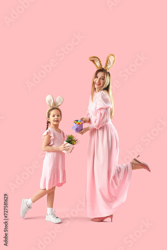 Cute little girl and her mother in bunny ears with Easter eggs on pink background