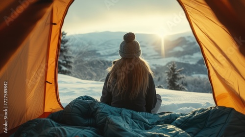 Relaxed female adventurer wakes up camping in the mountains, blanket, with snow.