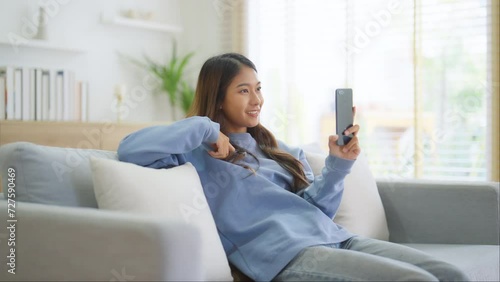 Wallpaper Mural Happy young asian woman relaxing at home. Female smiling and talking chat with friend sitting on sofa and holding mobile smartphone. Girl using video call to close friend Torontodigital.ca