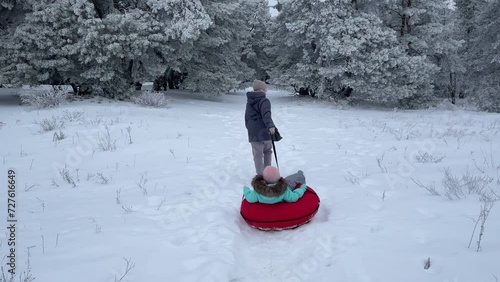 A young mother and son have fun in the winter in the forest sledding in slow motion. happy mom on a walk with her son in a snowy forest