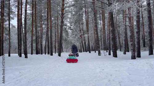 A young mother and son have fun in the winter in the forest sledding in slow motion. happy mom on a walk with her son in a snowy forest