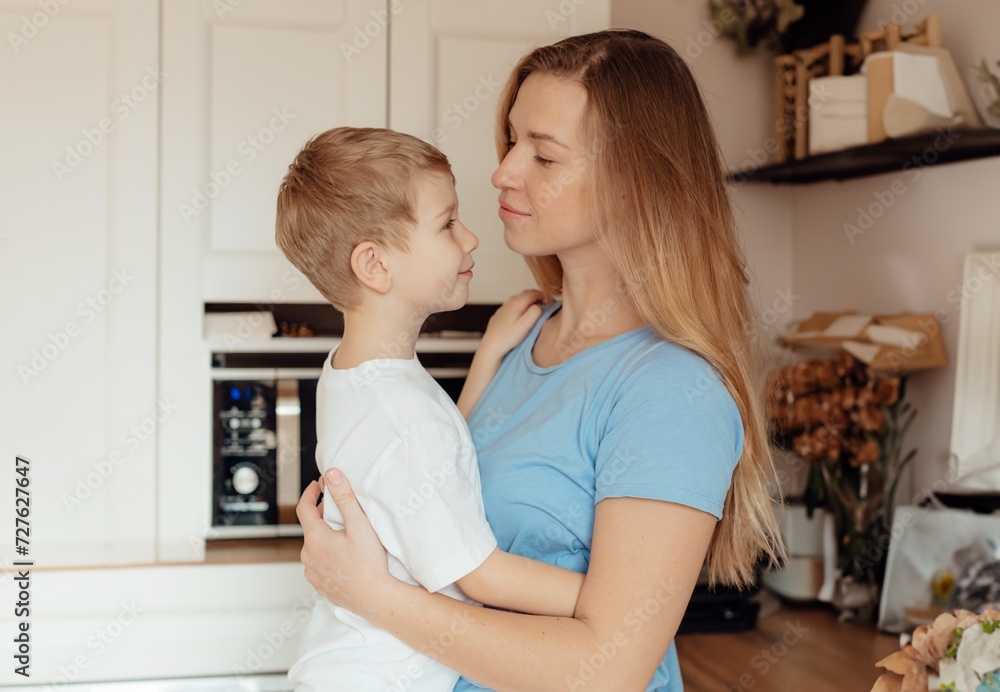 Happy mother and son smiling at each other affectionately. Young mother playing and hugging her cute son in the kitchen at home. Caring single mother bonding with her young son Happy mother and son smiling at each other affectionately. Young mother playing and hugging her cute son in the kitchen at home. Caring single mother bonding with her young son