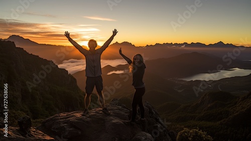 Triumphant couple celebrating success on mountain top by raising hands in the air