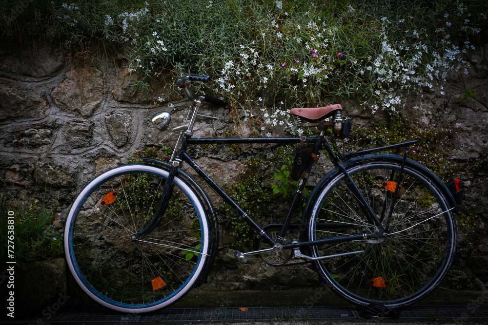 A vintage or retro,old black bike or bicycle with a brown seat,against a stone wall,Hallstatt,Austria