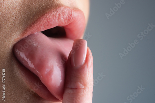 Tongue out licking finger with nails manicure. Closeup of female sticking tongue out. Macro tongue lick finger. Close up of woman mouth with tongue. Sexy tongues. Sensual finger lick.