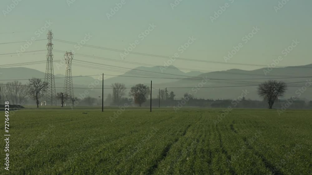 Misty fields with power lines and distant mountains at sunrise, serene landscape Misty fields with power lines and distant mountains at sunrise, serene landscape