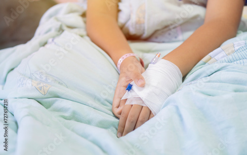 Young patient asian boy sitting on bed in hospital with IV saline drip to back of the hand, teenager sick in hospital