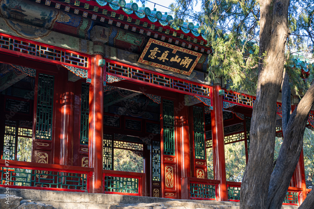 A large Chinese gazebo structure with open doors and windows, adorned with dense sculptures and ornaments surrounding a Chinese writing that translates 