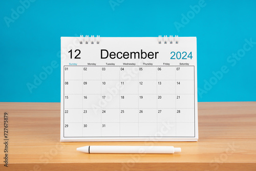 December monthly desk calendar for 2024 year and pen on wooden table with blue background.