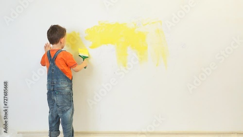 Kid painting with yellow the white wall of his room photo