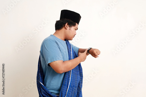 Side view of asian muslim boy standing while checking his wrist watch seriously photo