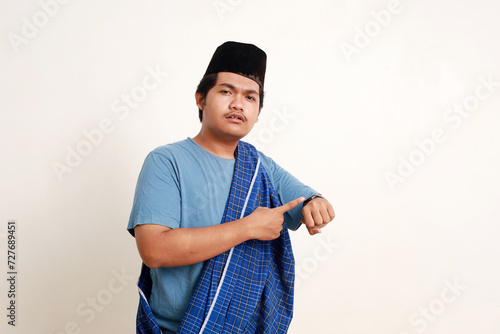 Asian muslim boy standing while pointing his wrist watch seriously photo