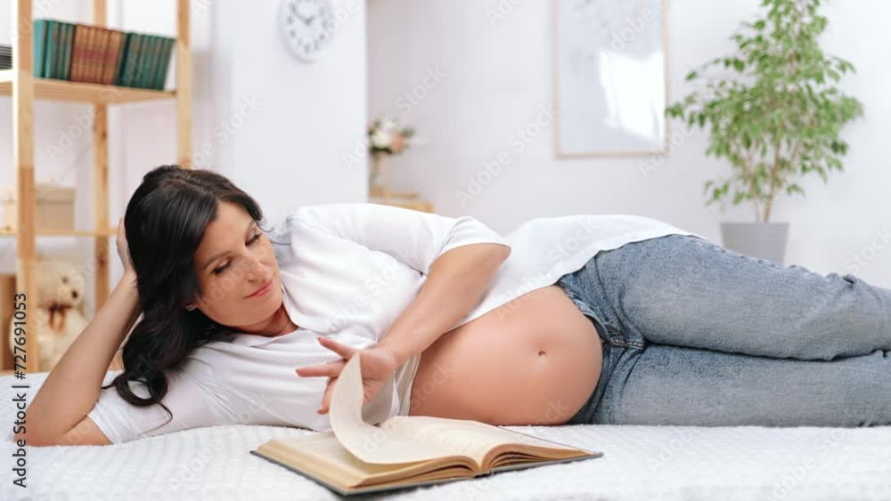 Happy middle-aged woman is eight months pregnant relaxing in bedroom, lying on bed and reading book Happy middle-aged woman is eight months pregnant relaxing in bedroom, lying on bed and reading book