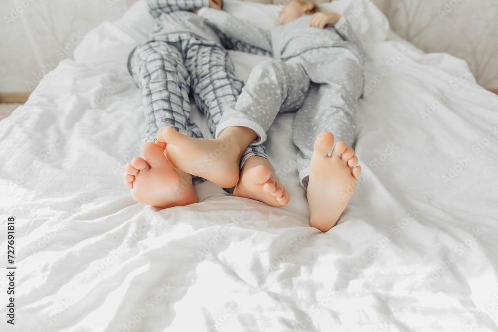 the bare, clean feet of two children, offspring, lying side by side under the same blanket on the bed. morning relaxation, cozy rest. cute pictures of baby feet