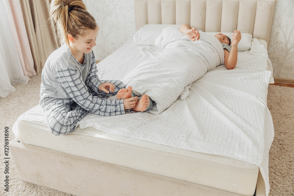 the children are wrapped in a blanket and tickling each other's heels on the bed. Family having fun at home. Leisure the children are wrapped in a blanket and tickling each other's heels on the bed. Family having fun at home. Leisure