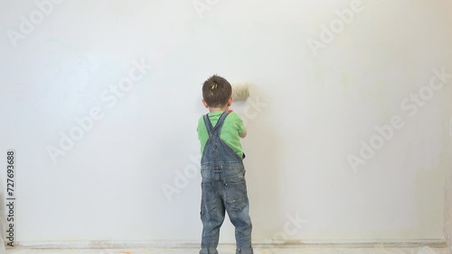 Little kid with big brush roller painting the wall in white