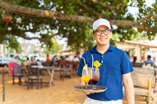 Portrait of Asian man waiter serving food and drink to customer on the table at tropical beach cafe and restaurant on summer holiday vacation. Food and drink business service occupation concept.