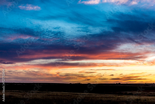 Fototapeta Naklejka Na Ścianę i Meble -  Sunrise or sunset in the Russian steppe at golden hour. Stratus, Cirrocumulus and Altocumulus clouds. The sun is shining from behind a cloud. Red orange and white shades. Morning or evening.