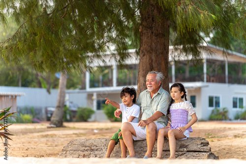 Happy Asian family enjoy and fun outdoor activity lifestyle travel ocean on summer beach holiday vacation. Grandfather and grandchild kids relaxing together on tropical island beach at sunset.