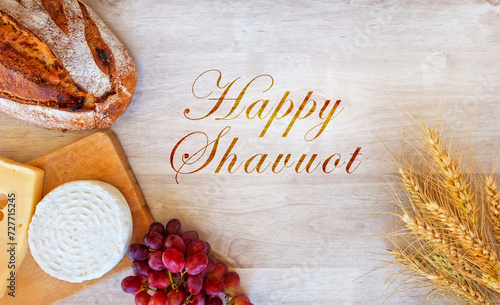Shavuot Jewish holiday, barley wheat with cheeses next to rustic bread and red grapes on a light white wooden surface background. a greeting for happy Shavuot