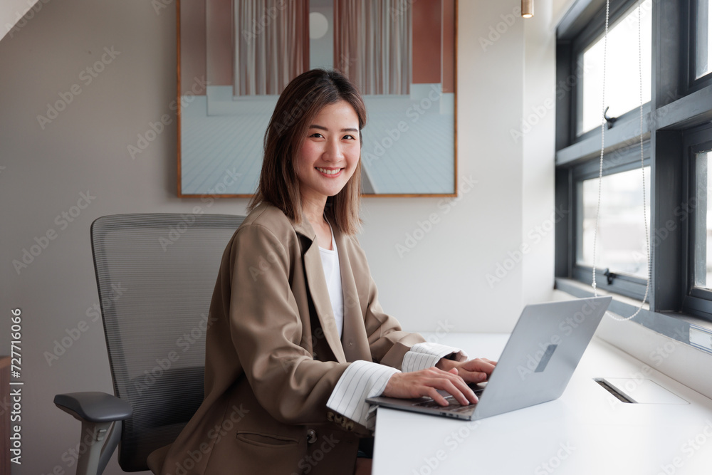 Happy brunette business lady using laptop, smiling at camera, posing for work, sitting in office in modern office Successful entrepreneurs and careers ke Happy brunette business lady using laptop, smiling at camera, posing for work, sitting in office in modern office Successful entrepreneurs and careers ke