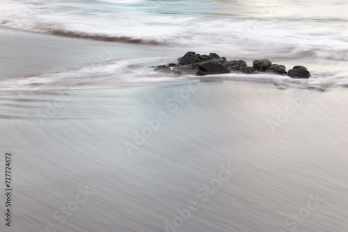 Long exposure waves moving over sand with rocks in background
