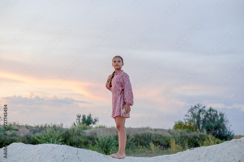 A teenage girl with long hair tied up in a ponytail short dress walks along a deserted canyon.