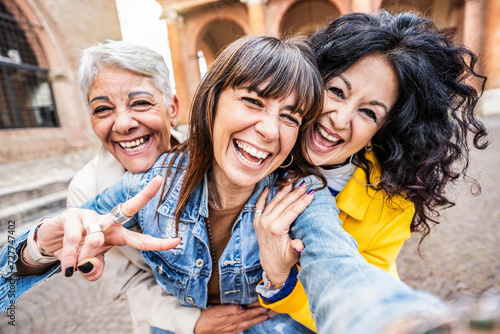Three senior women taking selfie photo with smart mobile phone device outside - Happy aged people having fun together walking on city street - Life style concept with mature females hanging out